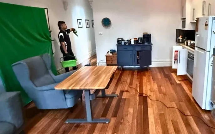 An "after" shot of a tidy open-plan room with a person performing final cleaning; the space is free of debris, featuring a neat desk and a clear kitchen.