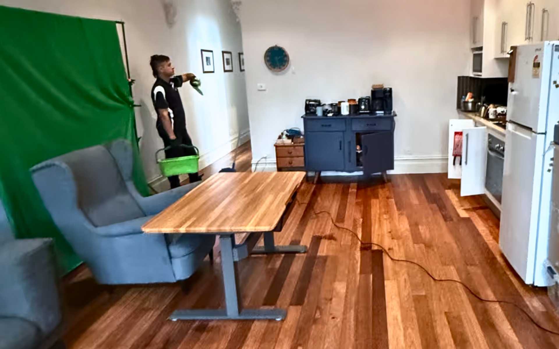 An "after" shot of a tidy open-plan room with a person performing final cleaning; the space is free of debris, featuring a neat desk and a clear kitchen.