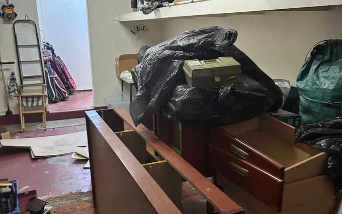 Estate and home clear out of a storage room filled with broken furniture and piled garbage bags.