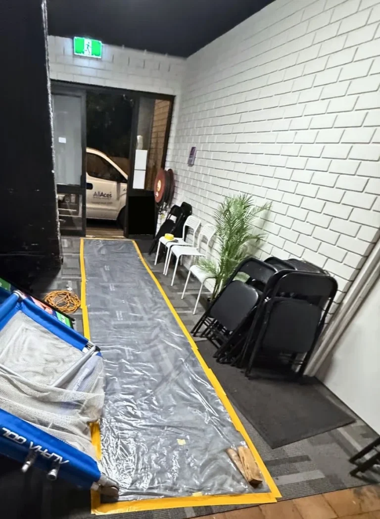 Water damage restoration team setting up protective plastic walkway sheeting inside a commercial hallway, with an AllAces van parked outside.