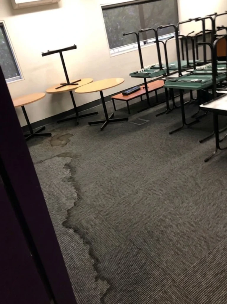 Commercial carpet water damage restoration Melbourne with stacked office tables and wet carpet tiles from a pipe leak.